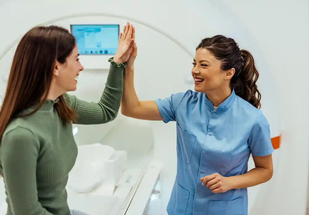 Technician high-five's a patient in front of an MRI machine